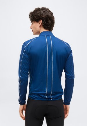 Homme de dos portant une veste de cyclisme à manches longues bleue avec des bandes réfléchissantes et un pantalon de cyclisme noir avec rembourrage.