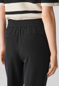 Schwarze Hose mit einem elastischen Bund, ausgestattet mit zwei Gesäßtaschen und einer glatten Textur, kombiniert mit einem gestreiften Strickoberteil.