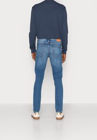 Vaqueros azul denim de corte ajustado con lavado desgastado, que cuentan con cinco bolsillos y una etiqueta de cuero con la marca en la parte trasera de la cintura. Combinados con una sudadera azul marino.