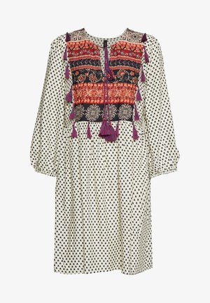 Robe blanche à motif de cœurs noirs, avec corsage brodé coloré orné de pampilles. Manches longues et coupe décontractée. Texture de tissu douce.