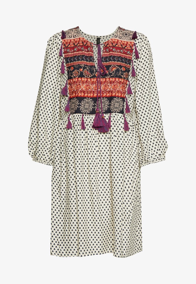 Robe blanche à motif de cœurs noirs, avec corsage brodé coloré orné de pampilles. Manches longues et coupe décontractée. Texture de tissu douce.