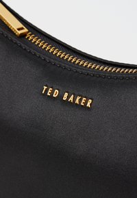 Ted Baker juodas satino krepšys su auksine užtrauktuko detale ir įspaustu logotipu. Lygus paviršius, elegantiškas dizainas ir kontrastinga aparatūra.