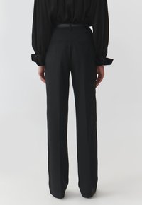 Pantaloni neri a vita alta con una vestibilità sartoriale, gambe dritte e tasche posteriori. Il materiale sembra liscio con una leggera lucentezza.