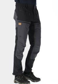 Mustat ja harmaat ulkoiluhousut, joissa on useita vetoketjullisia taskuja, joustava vyötärö ja vahvistetut alueet kestävyys varten. Yhdistetty mustiin vaelluskengiin.