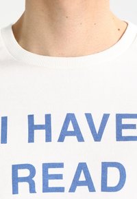 Weißes Baumwoll-T-Shirt mit Rundhalsausschnitt, das in fettblauer Schrift "ICH HABE GELESEN" zeigt. Rippkragen und weiche Textur sind offensichtlich.