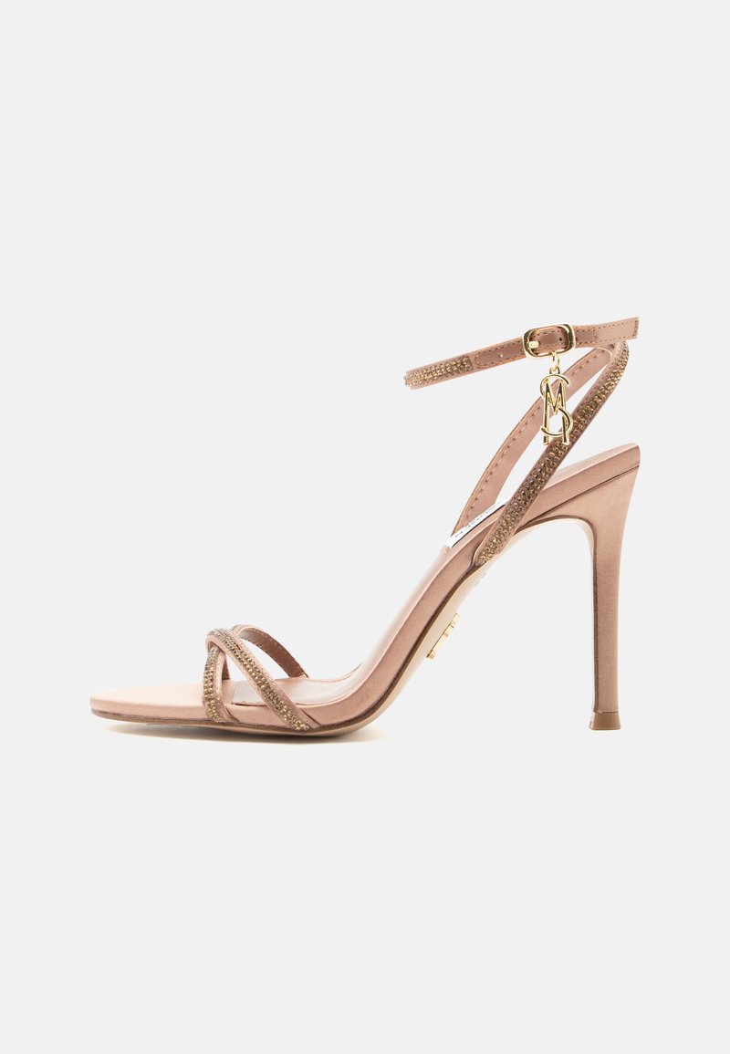 Γυμνό πέδιλο με ψηλό τακούνι, λεπτές λουρίδες, αγκράφα στον αστράγαλο και χρυσή λεπτομέρεια με μενταγιόν σε λευκό φόντο.