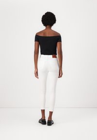 Top negro sin mangas combinado con jeans skinny blancos. Los jeans tienen bolsillos traseros y una etiqueta de cuero marrón en la cintura. Zapatos negros.