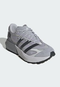 Gray athletic shoe with a textured upper, featuring black stripes and purple accents. Thick sole with rugged tread for traction.