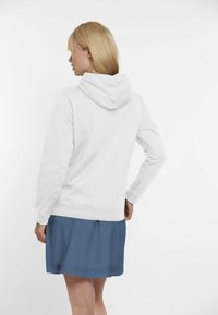 Vit hoodie med dragsko på huvan och ribbade ärmslut, kombinerad med en blå kjol. Slät tyg, avslappnad design och en ledig passform.