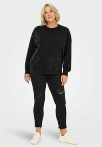 Svart sweatshirt med hjärtformade nitar, avslappnad passform, kombinerad med svarta ripped skinny jeans och vita sneakers. Avslappnad outfit.