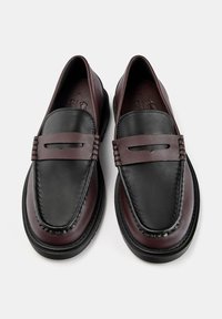 Sorte og burgunder læder loafers med en glat tekstur, der har et fremtrædende sadelrem og subtile syninger langs kanterne.