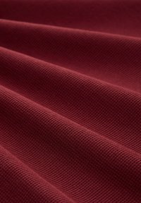Tessuto bordeaux testurizzato con un motivo a coste, caratterizzato da più pieghe che creano un aspetto ondulato. Il materiale appare morbido e resistente.