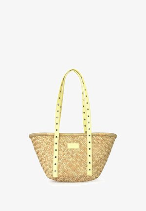 Sac cabas en paille tressée avec de longues anses jaunes décorées d'œillets métalliques et une petite étiquette rectangulaire sur le devant.
