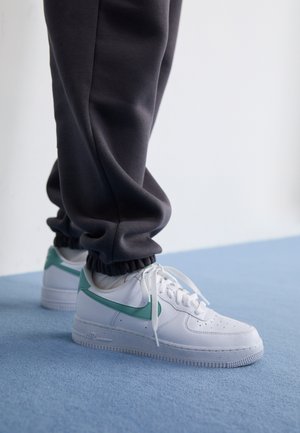 Vita Nike Air Force 1-sneakers med en mintgrön swoosh, texturerad läderöverdel och vita snören, kombinerade med mörkgrå uppvikta joggers.