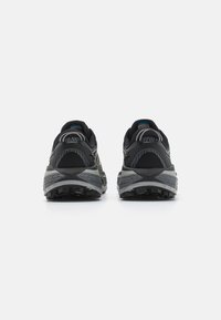 Des chaussures de course noires avec une tige en maille texturée, des accents gris et des semelles en caoutchouc robustes avec un profil de traction multidirectionnel.