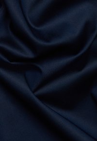 Granatowy materiał o gładkiej, błyszczącej teksturze, z delikatnymi fałdami i subtelnym połyskiem, podkreślający jego płynne ułożenie i elegancki wygląd.