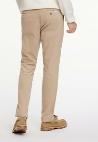 Beige, slim-fit trousers with a subtle texture, featuring two back pockets and a small brand tag. Paired with tan shoes.