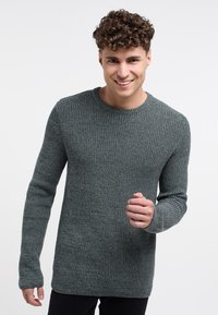 Maglione grigio a costine con maniche lunghe e scollatura rotonda. Texture liscia, forma aderente e dettagli di motivo sottili in tutto il capo.
