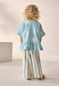 Svetlo modra peplum bluza z belimi cvetličnimi vzorci, kombinirana s širokimi hlačami z belimi, modrimi in rjavimi črtami. Sandali zaokrožajo videz.