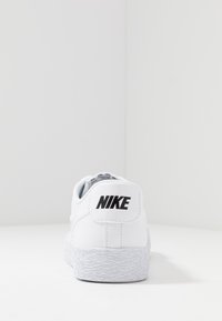 Nike sneakers med ett överviktigt vitt läderövre, texturerad vit sula och en svart logotyp på hälfliken.