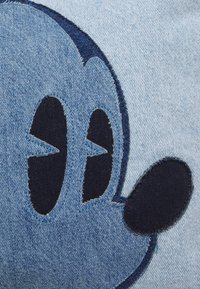 Blå denimtyg med ett stort, mörkblått broderat ansikte av en tecknad karaktär med framträdande ögon och en cirkulär näsa.