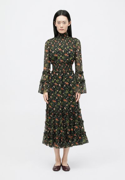 Vestido negro con estampado floral, mangas largas, puños con volantes y diseño en capas. Presenta flores vibrantes y una cintura fruncida. Se lleva con zapatos planos burdeos.
