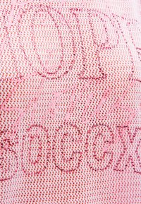 Nahaufnahme von pinkem Netzstoff mit schimmernden pinken Strasssteinen, die abstrakte und geschwungene Textmuster bilden.
