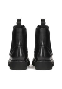 Botines de piel negra con una textura suave, punta redondeada y suela de goma plana. Presentan tiradores en la parte trasera para facilitar su puesta.