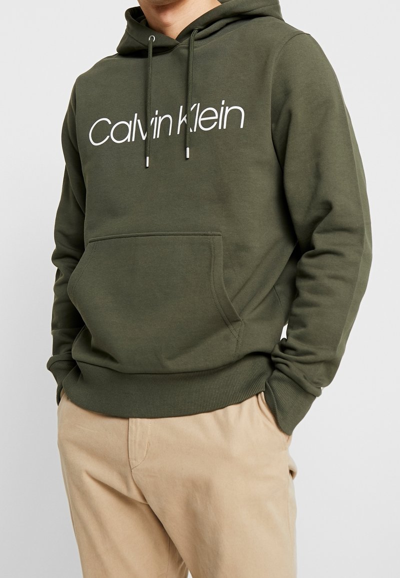Felpa con cappuccio verde oliva in misto cotone. Presenta una tasca a marsupio sul davanti e testo del logo bianco. Polsini e orlo ribassati.