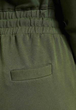 Grüner Strickstoff mit einem elastischen Bund, der ein horizontales Taschendesign aufweist. Glatte Textur mit leichtem Glanz.