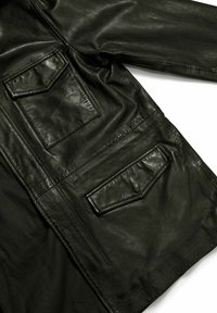 Giacca di pelle nera con due tasche sul petto con chiusura a patta, texture liscia e dettaglio di cucitura visibile lungo le maniche e i lati.