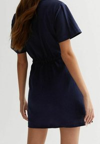 Mörkblå klänning med korta ärmar och elastisk midja, mitt på låret längd, och ett slätt, något texturerat tyg.