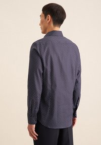 Marineblauwe shirt met een wit stippenpatroon, lange mouwen en een geknoopt kraag. Heeft een gebogen zoom en een gladde stofstructuur.