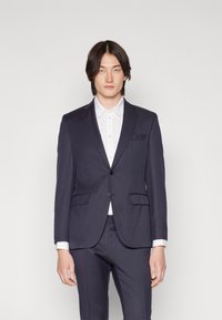 Navy suit jacket with notch lapels and two front pockets, paired with a white collared shirt. Smooth texture and tailored fit.