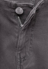 Primo piano di un tessuto in denim grigio scuro con una cerniera metallica aperta e un bottone metallico etichettato "DENIM AUTHENTIC".