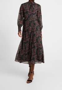 Pitkä, tummanvihreä mekko, jossa on pinkkejä ja punaisia kukkakuoseja. Sisältää korkean kauluksen, pitkät hihat ja hulmuavan helman. Mustat remmi-korkokengät.