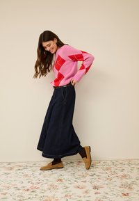 Ružičasti i crveni argyle džemper, tamna traper maksi suknja i smeđe mokasine. Ima dugačke rukave i opušteni kroj. Pod s cvjetnim uzorkom.