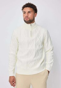 Pull blanc en tricot avec un col montant et une fermeture à demi-fermeture éclair, présentant un motif losange en relief ainsi que des poignets et un ourlet côtelés.