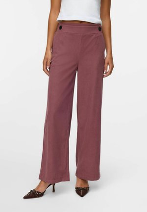 Pantalons évasés en tissu mauve doux, présentant une taille haute avec des boutons sur le devant et une texture lisse. Associés à des talons aiguilles marron.