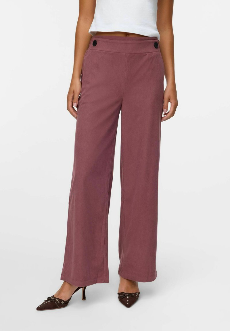 Vidjejeans i ett mjukt mauve-tyg, med hög midja och framknappar samt en slät textur. Matchat med spetsiga bruna klackar.