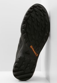 Musta urheilukenkä, jossa on teksturoidut pito-kuviot ja erittäin näkyvä oranssi 'Continental' -logo. Sisältää Adidas-brändäystä.