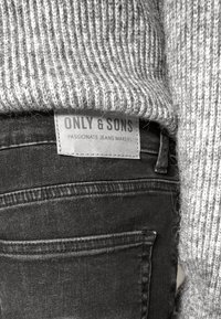 Suéter gris de punto con canalé vertical, combinado con jeans de mezclilla negros. La etiqueta visible muestra "ONLY & SONS" con "MAKERS DE JEANS APASIONADOS."