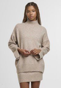 Bézs kötött pulóver magas nyakkal, oversized fazonnal, bordás alsó résszel és hosszú ujjakból áll. Puha textúra, laza dizájn, réteges megjelenéssel.