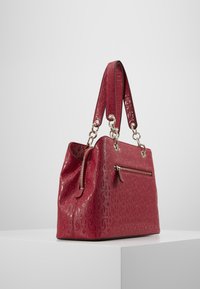 Sac à main en cuir rouge avec motif embossé, ferrures argentées, deux anses, poche zippée latérale et forme structurée.