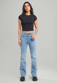 Schwarzes, verkürztes T-Shirt mit kurzen Ärmeln, kombiniert mit hellblauen ausgestellt geschnittenen Jeans. Die Jeans verfügen über ein klassisches Fünf-Taschen-Design und einen Knopfverschluss.