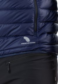 Marineblaue isolierte Jacke mit einer gepolsterten Design, ausgestattet mit dem "Premium Down" Logo, seitlichen Reißverschlusstaschen und schwarzen Stoffakzenten am unteren Rand.