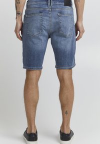 Pantalones cortos de denim en azul claro con un efecto desgastado, que presentan un diseño clásico de cinco bolsillos y puños enrollados, combinados con zapatillas negras.