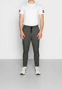 Gråternet joggingbukser med elastisk talje og snor, parret med en enkel hvid t-shirt med sorte striber på ærmerne.