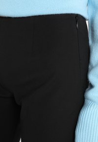 Zwarte broek met een zachte textuur, voorzien van een zijrits, gecombineerd met een lichtblauwe gebreide trui met geribbelde manchetten.