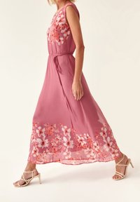 Robe maxi rose avec imprimé floral à l'ourlet, design sans manches, taille cintrée avec un lien, tissu doux et fluide, et texture légère.